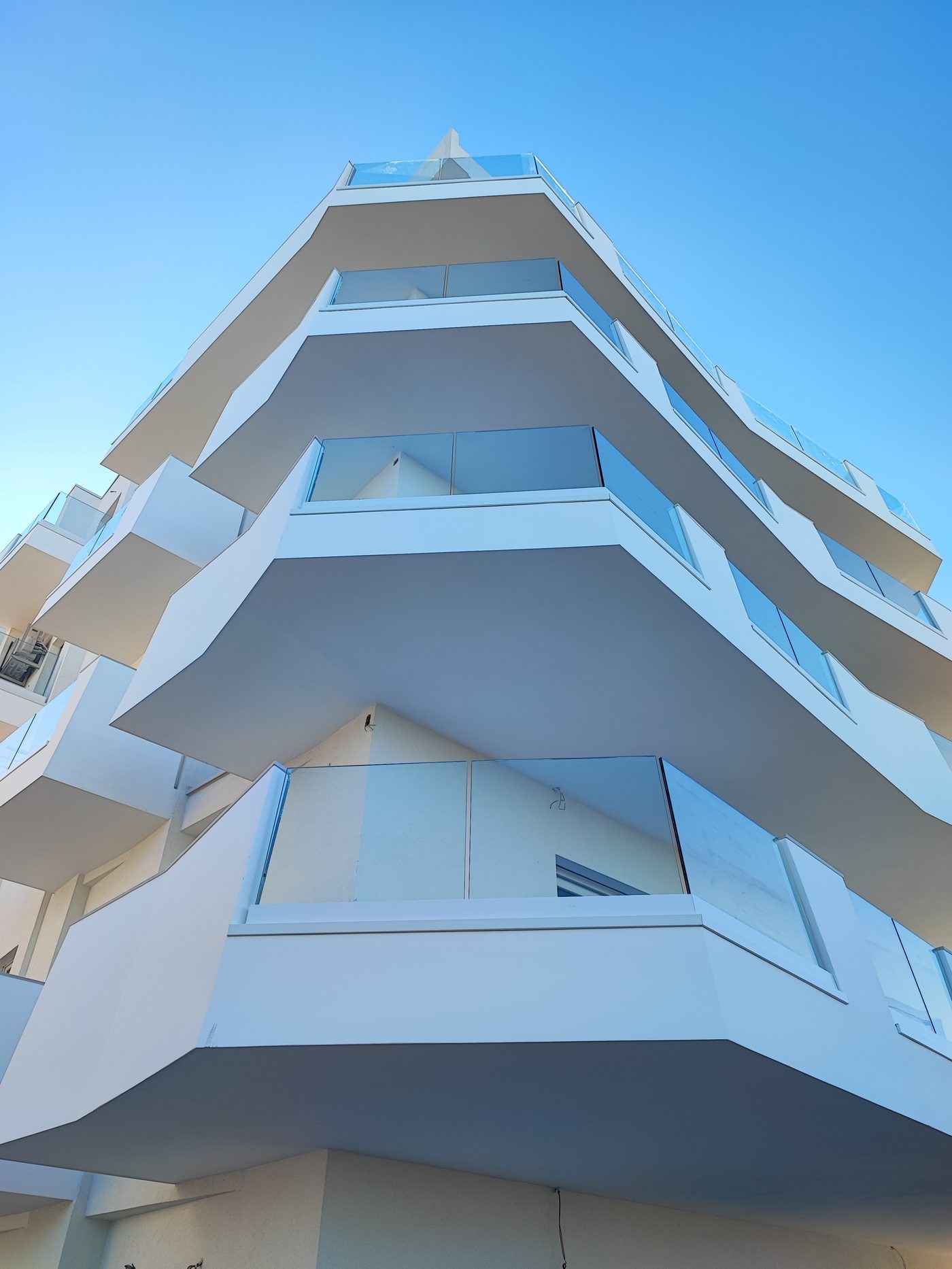 Dettaglio dal basso dei balconi con balaustre in vetro a fissaggio puntuale, edificio residenziale ad Alba Adriatica
