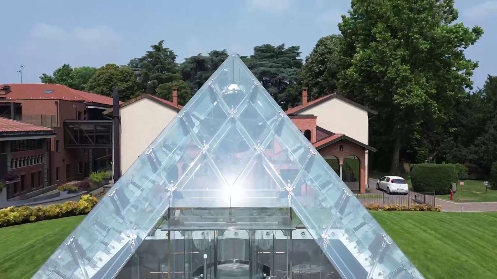 Ripresa aerea frontale dell'apice della Glass Pyramid a Carate Brianza, con il parco e gli edifici storici sullo sfondo