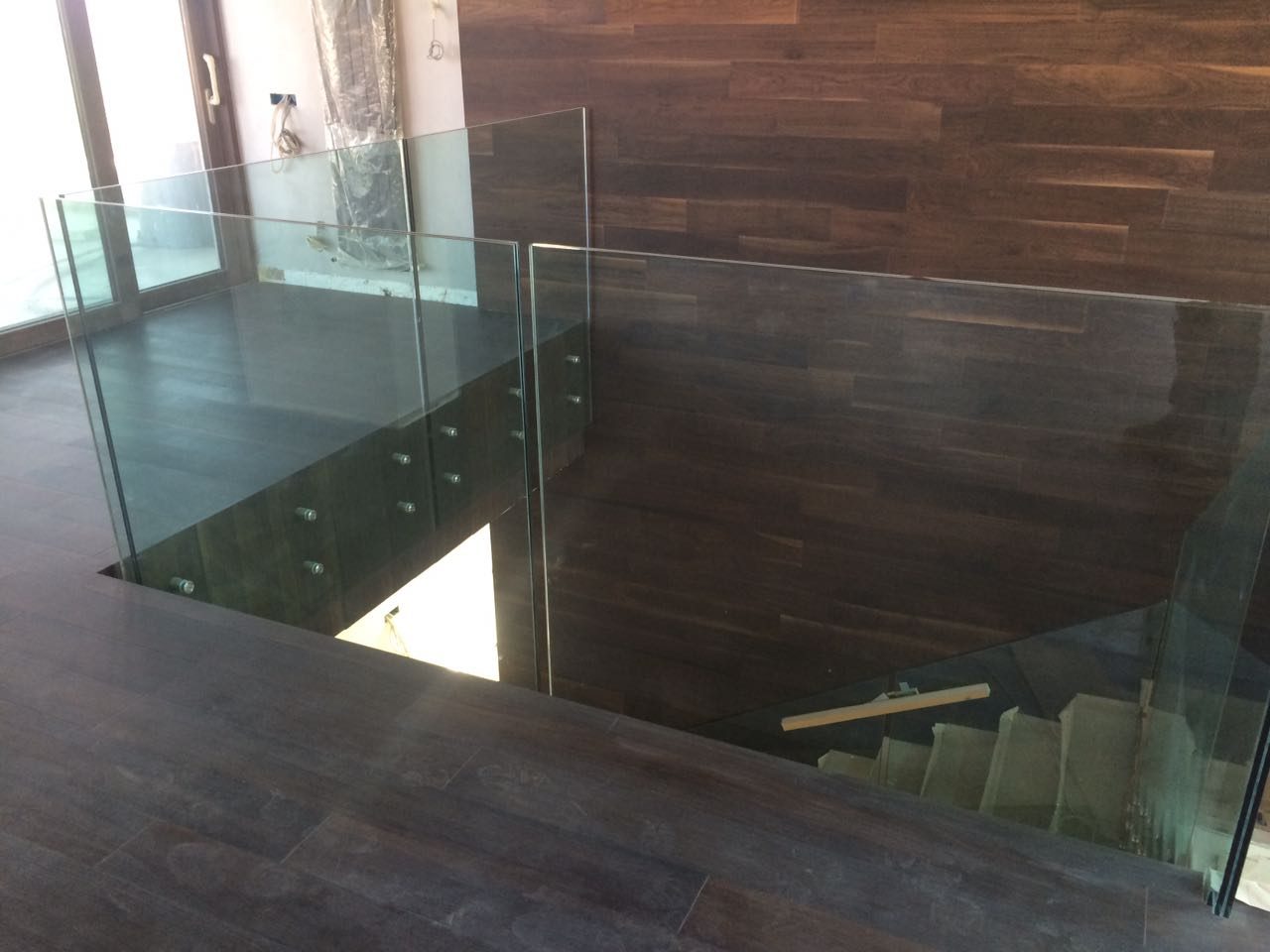 Balaustra in vetro a protezione di un'apertura nel solaio, con fissaggio puntuale su pavimento in legno scuro, cantiere a Baku