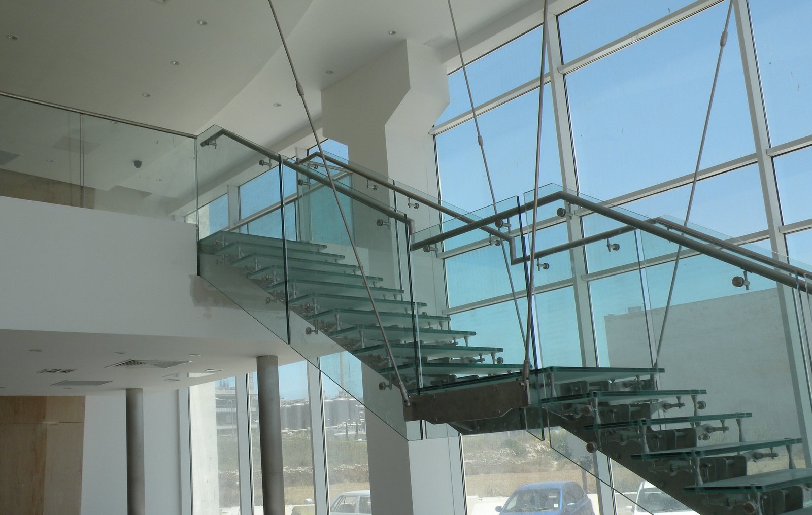 Scala interamente in vetro sospesa a tiranti d'acciaio in uno showroom con vetrate a tutta altezza, Malta